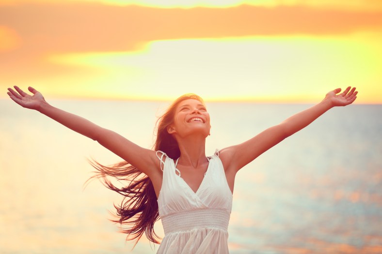 Free happy woman arms up praising freedom at beach sunset. Young